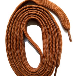 Op de afbeelding: Opgerolde bruine veters met een getextureerde, geweven uitstraling. De veters hebben een effen, warme bruine kleur en plastic veteroogjes aan elk uiteinde. De veters zijn ontworpen voor schoenen en laarzen.