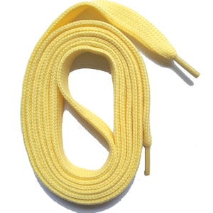 Könnte beinhalten: Ein Paar hellgelbe Schnürsenkel, auf weißem Hintergrund aufgerollt. Die Schnürsenkel sind flach und aus gewebtem Material gefertigt, mit den Aglets an den Enden. Die Schnürsenkel haben eine hellgelbe Pastellfarbe.