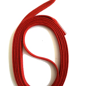 May include: A single, coiled red shoelace against a white background. The shoelace is flat and has a woven texture. The aglet, the plastic or metal tip, is visible at the end of the lace.
