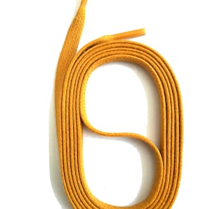 Può includere: Stringhe giallo senape, piatte e intrecciate, arrotolate su sfondo bianco. I puntali sono di una tonalità di giallo più chiara. Adatte per sneakers, stivali o altre calzature.