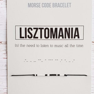 May include: A black and white beaded bracelet with the word "LISZTOMANIA" and the definition "(n) the need to listen to music all the time." in black text on a white card. The bracelet is made with black and white beads and a black string.