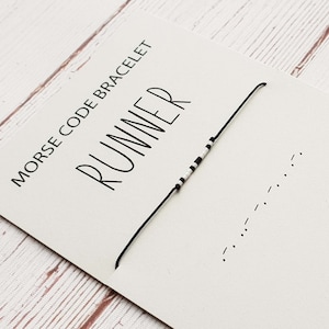Pode incluir: Um bracelete de contas pretas e brancas com a palavra "RUNNER" escrita em um cartão. O bracelete é um bracelete de código Morse, e o cartão mostra o código Morse para a palavra "RUNNER".