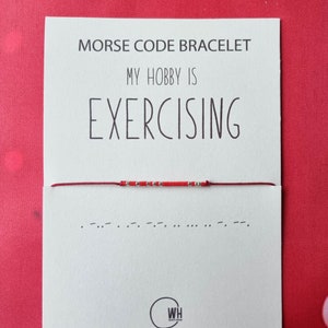 Può includere: Braccialetto di corda rossa con perline argentate che compongono la parola "Exercising" in codice Morse. Il braccialetto è su una carta bianca con il testo "Morse Code Bracelet My Hobby Is Exercising".