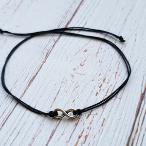 Puede incluir: Un brazalete de cuerda negra con un dije de plata en forma de infinito.