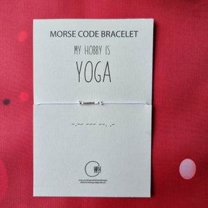 May include: White string bracelet with gold beads spelling out "YOGA" in Morse code. The bracelet is on a white card with the text "Morse Code Bracelet, My Hobby Is YOGA".