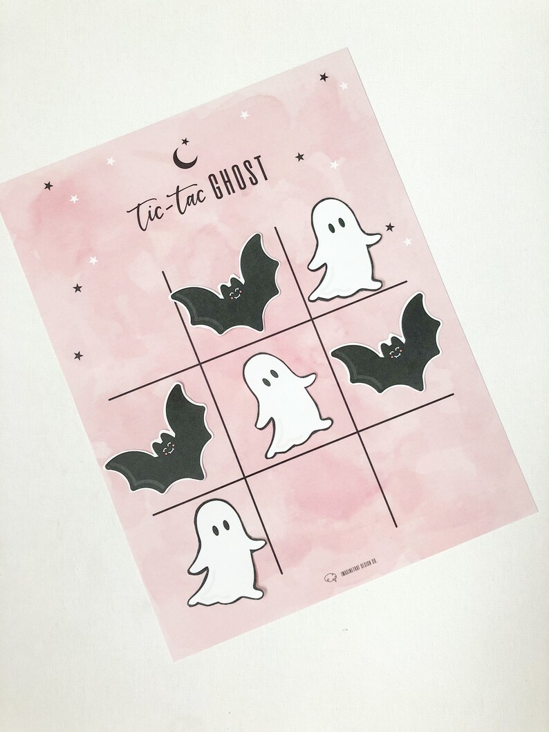 May include: A pink and white tic-tac-toe game board with the words "tic-tac GHOST" printed at the top. The game board has nine squares with images of ghosts and bats in each square.