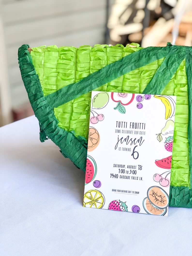 Puede incluir: Una invitaci&oacute;n colorida para una fiesta de cumplea&ntilde;os de 6 a&ntilde;os con tem&aacute;tica de frutas. La invitaci&oacute;n presenta una sand&iacute;a, una pi&ntilde;a, un pl&aacute;tano, un lim&oacute;n, una fresa y cerezas. El texto de la invitaci&oacute;n dice: "Tutti Frutti Ven a celebrar a nuestra querida Jensen que cumple 6 a&ntilde;os S&aacute;bado, 18 de agosto 13:00 a 15:00 1940 Cascade Falls Ln. &iexcl;Trae tu traje de ba&ntilde;o para nadar!"