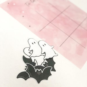 May include: A set of Halloween-themed stickers featuring black bats with white eyes and white ghosts with black eyes. The stickers are on a white background.