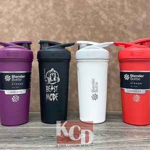 May include: Four BlenderBottle Strada shaker bottles in different colors: purple, black, white, and red. The bottles are insulated and have a  "BlenderBottle" logo and the text "STRADA" on them. The black bottle has a graphic of a gorilla lifting weights and the text "BEAST MODE".