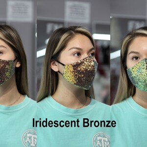 May include: A woman is wearing a face mask with iridescent bronze sequins. The mask has a teal and gold color scheme. The text "Iridescent Bronze" is below the image.