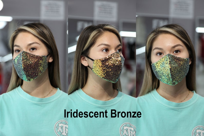 May include: A woman is wearing a face mask with iridescent bronze sequins. The mask has a teal and gold color scheme. The text "Iridescent Bronze" is below the image.