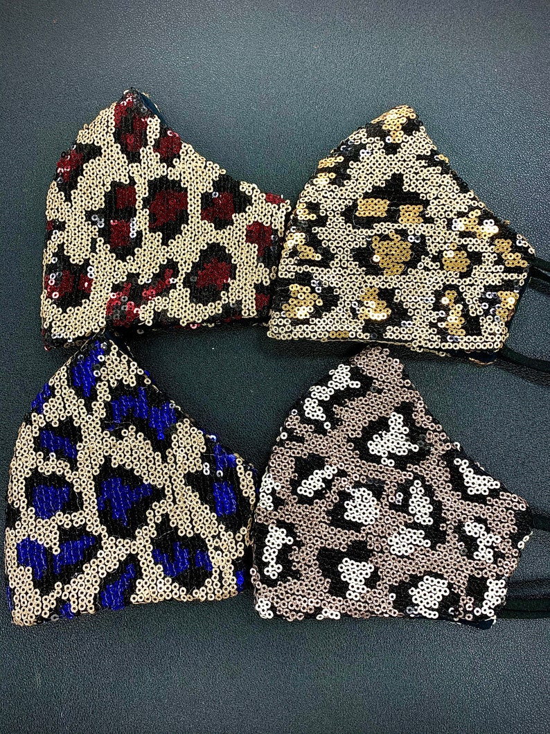 May include: Four sequined face masks with different animal print designs. The masks are black with gold, red, blue, and white sequins.