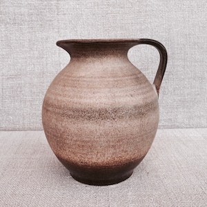 May include: A brown ceramic pitcher with a wide mouth and a handle. The pitcher has a textured surface and a dark brown glaze.