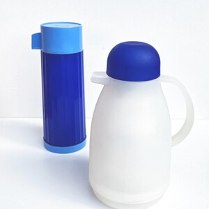 Puede incluir: Dos recipientes aislados para bebidas. Uno es un termo azul oscuro con tapa azul claro. El otro es una jarra blanca en forma de pera con tapa azul y asa. Ambos mantienen las bebidas calientes o frías.