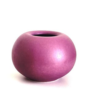 May include: A small, round, purple ceramic vase with a smooth, glossy finish.