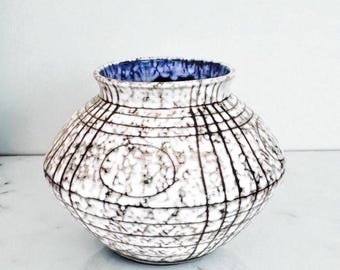 May include: A ceramic vase with a round body and a wide opening. The vase is white with a textured surface and a black grid pattern. The interior is blue. Decorative home decor.