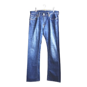 Op de afbeelding: Blauwe denim jeans hangend aan een metalen hanger. De jeans hebben een klassiek ontwerp met vijf zakken, een knoop- en ritssluiting en een vervaagde wassing. De jeans hebben een rechte pijp en lijken van een medium gewicht denim te zijn.