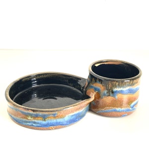 May include: A ceramic serving dish with a small dipping bowl attached. The dish is glazed in shades of blue, brown, and gold.