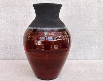 May include: A dark red ceramic vase with a black rim. The vase has a glossy finish and a rounded shape.