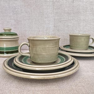 May include: A set of vintage ceramic teacups and saucers with green and brown stripes. The cups and saucers are in a light beige colour. There is also a matching sugar bowl with a lid.