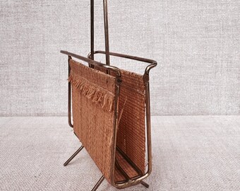 May include: A gold metal magazine rack with a woven brown fabric insert. The rack has a tall handle and three legs.