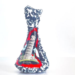 May include: A decorative vase with a textured, dark blue and white exterior. The interior features a red background with an image of the Leaning Tower of Pisa and the word "PISA".