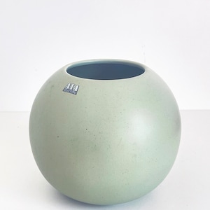 May include: A light green ceramic vase with a round shape. The vase has a label that says "ASA Selection".