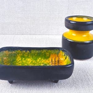 May include: A set of two black and yellow ceramic dishes. The larger dish is a vase with a wide mouth and a narrow base. The smaller dish is a rectangular tray with a green and yellow glaze. Both dishes have a glossy finish.