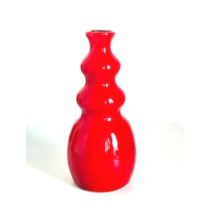 May include: A bright red ceramic vase with a unique, bulbous shape. The vase has a smooth, glossy finish and a wide opening at the top.
