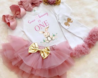 Puede incluir: Conjunto de fiesta para bebé que incluye un body blanco de manga larga con el texto "Some bunny is ONE" y un diseño de conejito, una falda tutú rosa y accesorios a juego. Con un lazo dorado, una diadema y un lazo.