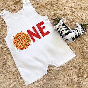 May include: White baby romper featuring a pizza illustration and the word "ONE" in red. The outfit includes black and white trainers. Ideal for a first birthday celebration.