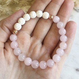 May include: A bracelet made with pink and white beads. The bracelet has a rose quartz and lava rock design.