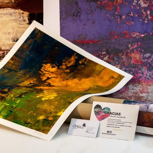 May include: A rolled up canvas print with a colorful abstract design in shades of yellow, green, and blue. The print is on a table next to a business card and a thank you note that says "Gracias" in Spanish.