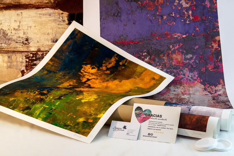 May include: A rolled up canvas print with a colorful abstract design in shades of yellow, green, and blue. The print is on a table next to a business card and a thank you note that says "Gracias" in Spanish.