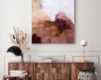 Puede incluir: Pintura abstracta en tonos marrones, rosas y blancos, colgada en una pared blanca sobre una cómoda de madera con dos pequeños taburetes de madera y una cesta tejida.