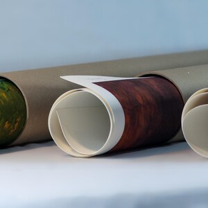 May include: Three rolled-up prints in brown cardboard tubes. The prints are visible on the ends of the tubes. The print on the left is a green and yellow landscape. The print in the middle is a red and brown landscape. The print on the right is a blue and white landscape.