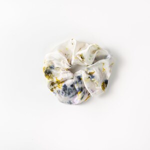 Puede incluir: Un scrunchie blanco con un patr&oacute;n floral en tonos amarillos, azules y morados.