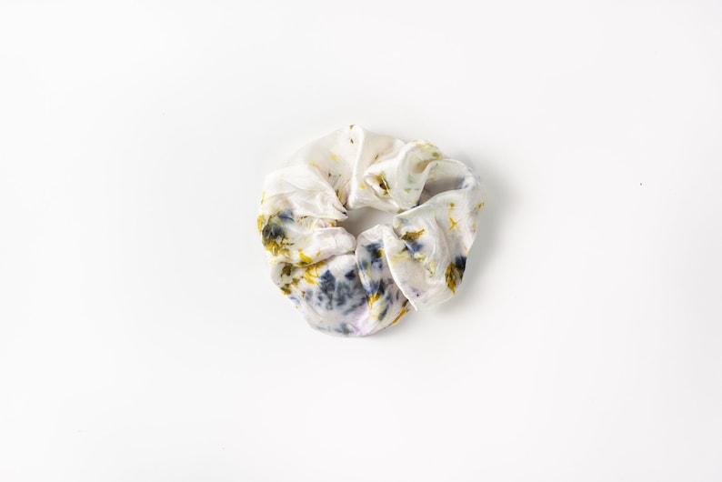 Puede incluir: Un scrunchie blanco con un patr&oacute;n floral en tonos amarillos, azules y morados.