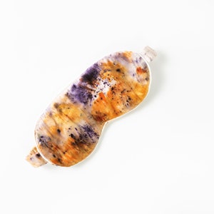 May include: A sleep mask made of silk with a tie-dye pattern in shades of purple, orange, and yellow.