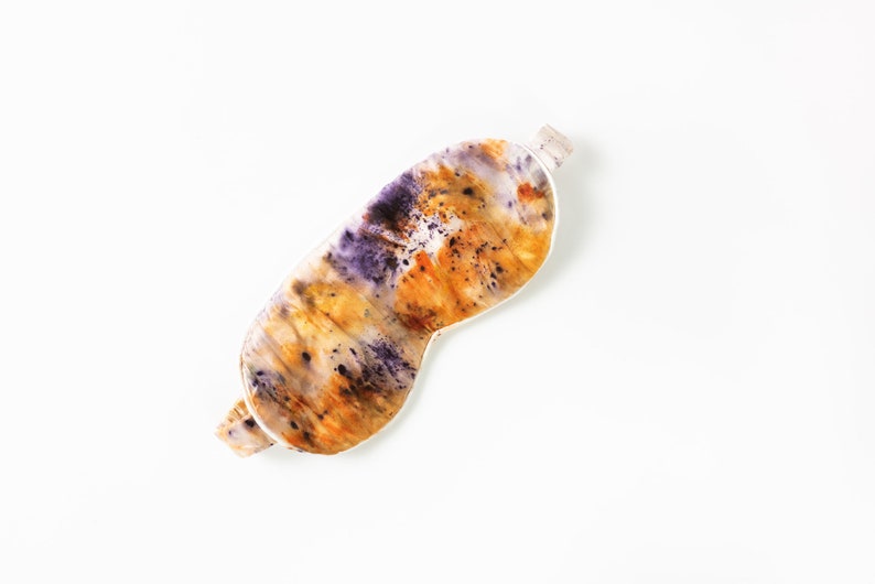 May include: A sleep mask made of silk with a tie-dye pattern in shades of purple, orange, and yellow.