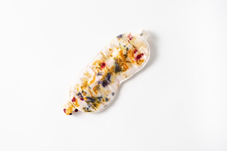 May include: A white silk sleep mask with a colorful floral pattern in shades of yellow, orange, red, and purple.