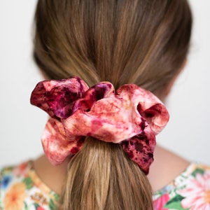 Puede incluir: Un scrunchie de pelo de color rosa y burdeos con estampado tie-dye.