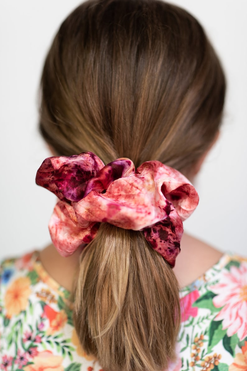 Puede incluir: Un scrunchie de pelo de color rosa y burdeos con estampado tie-dye.