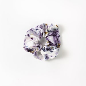 Puede incluir: Un scrunchie para el pelo de color blanco, morado y dorado.