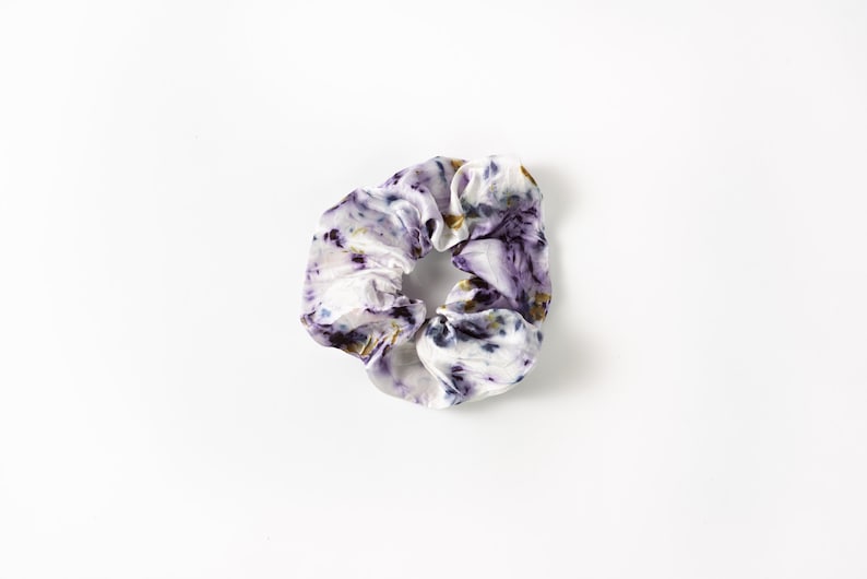 Puede incluir: Un scrunchie para el pelo de color blanco, morado y dorado.