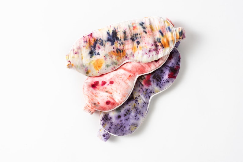 May include: Three colorful silk sleep masks with tie-dye patterns in shades of purple, pink, and yellow. The masks are stacked on top of each other.