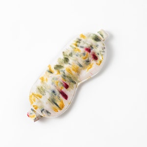 May include: A white sleep mask with a tie-dye pattern in shades of yellow, green, and red.