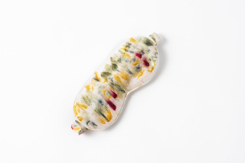 May include: A white sleep mask with a tie-dye pattern in shades of yellow, green, and red.