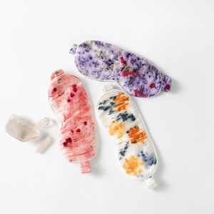 May include: Three colorful silk sleep masks with tie closures. The masks are decorated with tie-dye patterns in shades of purple, pink, and orange.