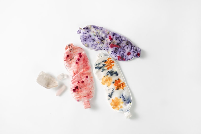 May include: Three colorful silk sleep masks with tie closures. The masks are decorated with tie-dye patterns in shades of purple, pink, and orange.